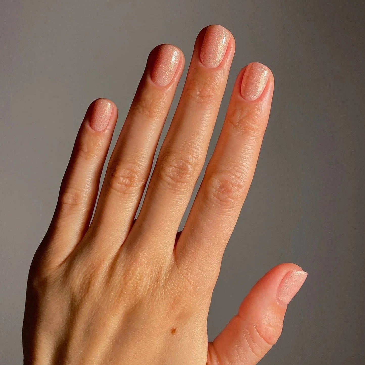 Close-up of a hand with neatly manicured nails against a neutral background