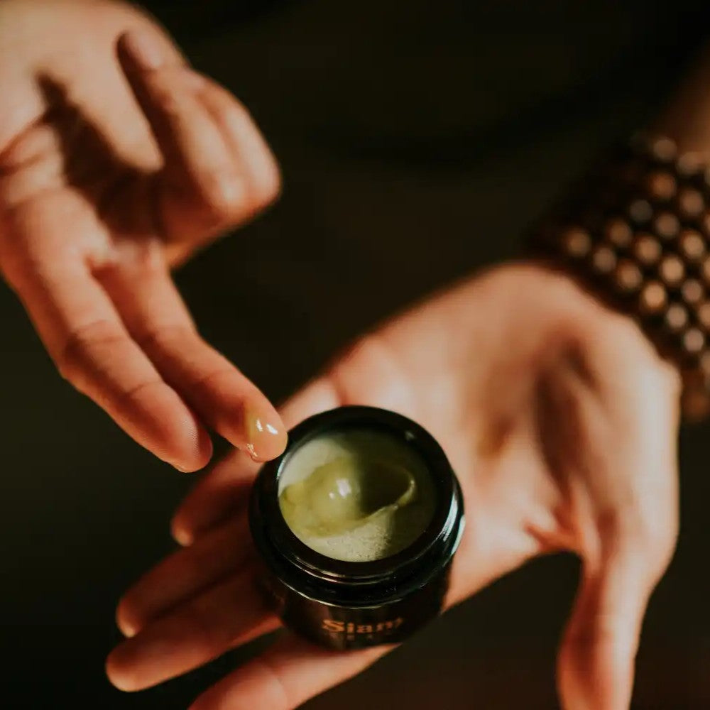 Person holding a jar of green SIAM SEAS SEAS Elements Beauty Balm with a blurred background