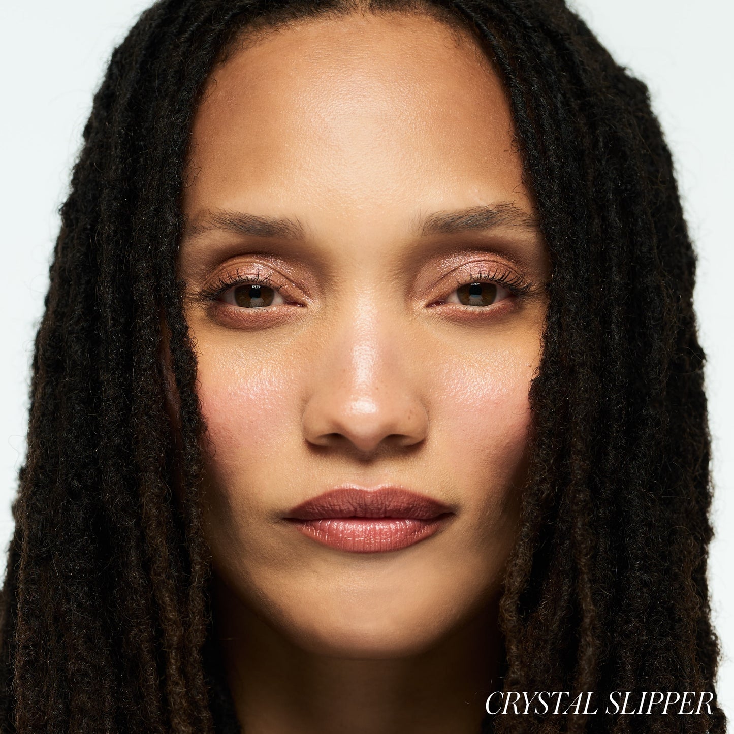 Close-up of a woman with dark hair against a white background wearing RMS BEAUTY Luminizer Crystal Slipper