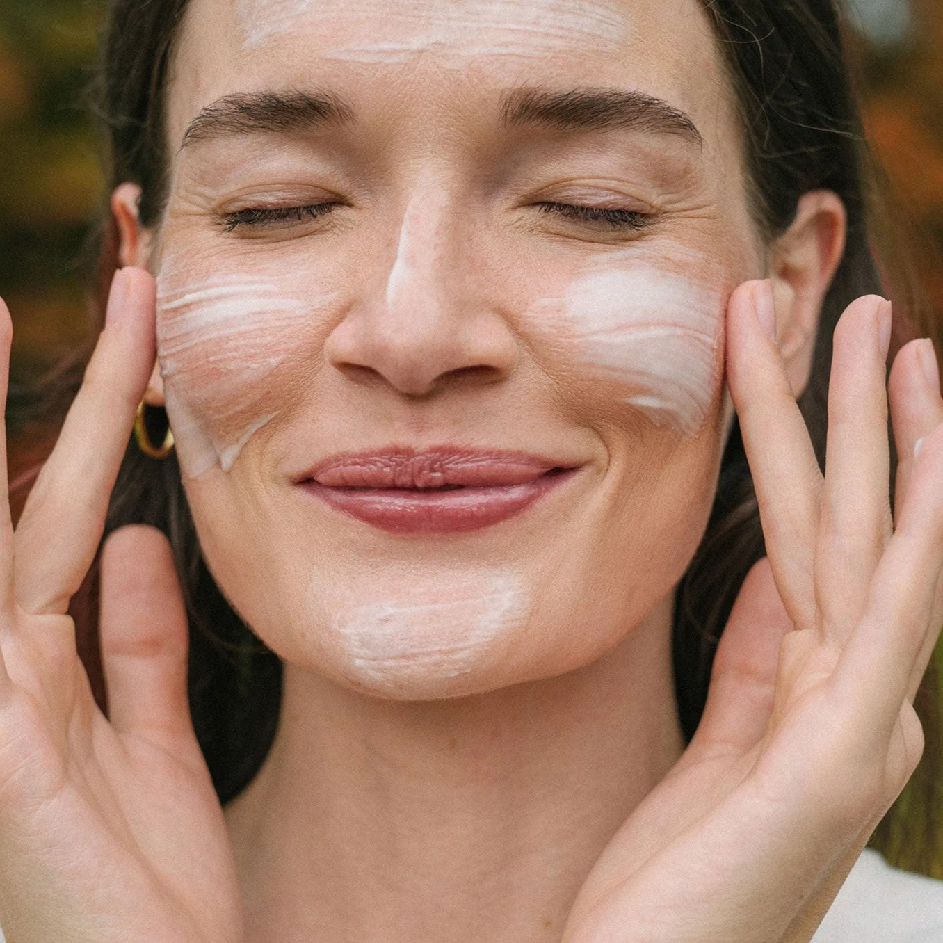 Woman applying URSA MAJOR Vital Spring Hydration Mask to her face with a blurred natural background