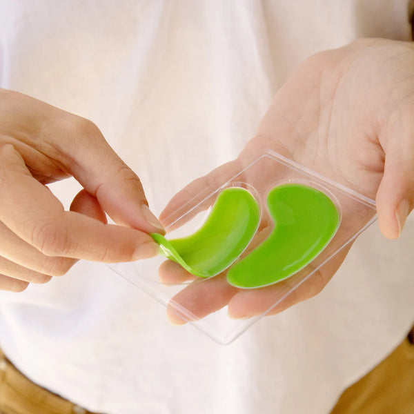 Green eye masks in a clear packaging held by hands against a white background