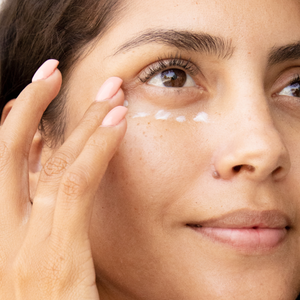Close-up of a person applying cream under their eye with a hand.