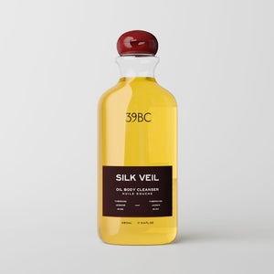 A 39BC Silk Veil oil body cleanser bottle filled with golden yellow liquid, featuring a dark brown label and a glossy dark red spherical cap, set against a light gray background.