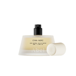 A frosted glass perfume bottle with a black spray top and a detached white cap, shown on a clean white background. The bottle label reads 'CYAN NORI' and 'Abel'.