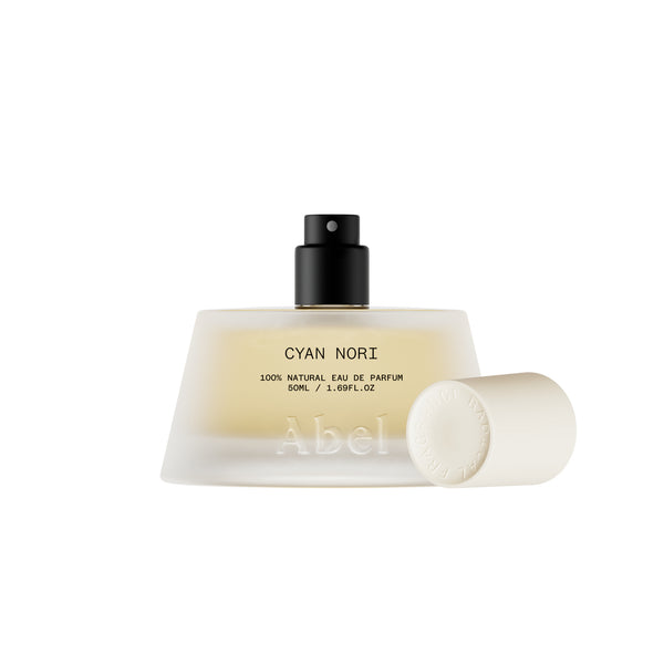 A frosted glass perfume bottle with a black spray top and a detached white cap, shown on a clean white background. The bottle label reads 'CYAN NORI' and 'Abel'.