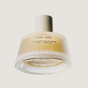 A frosted glass perfume bottle with a metallic silver cap, labeled 'CYAN NORI' and 'Abel', shown against a solid light beige background.
