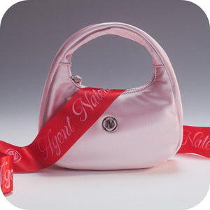 Pink handbag with a red ribbon and 'Agent Nateur' branding on a gray background