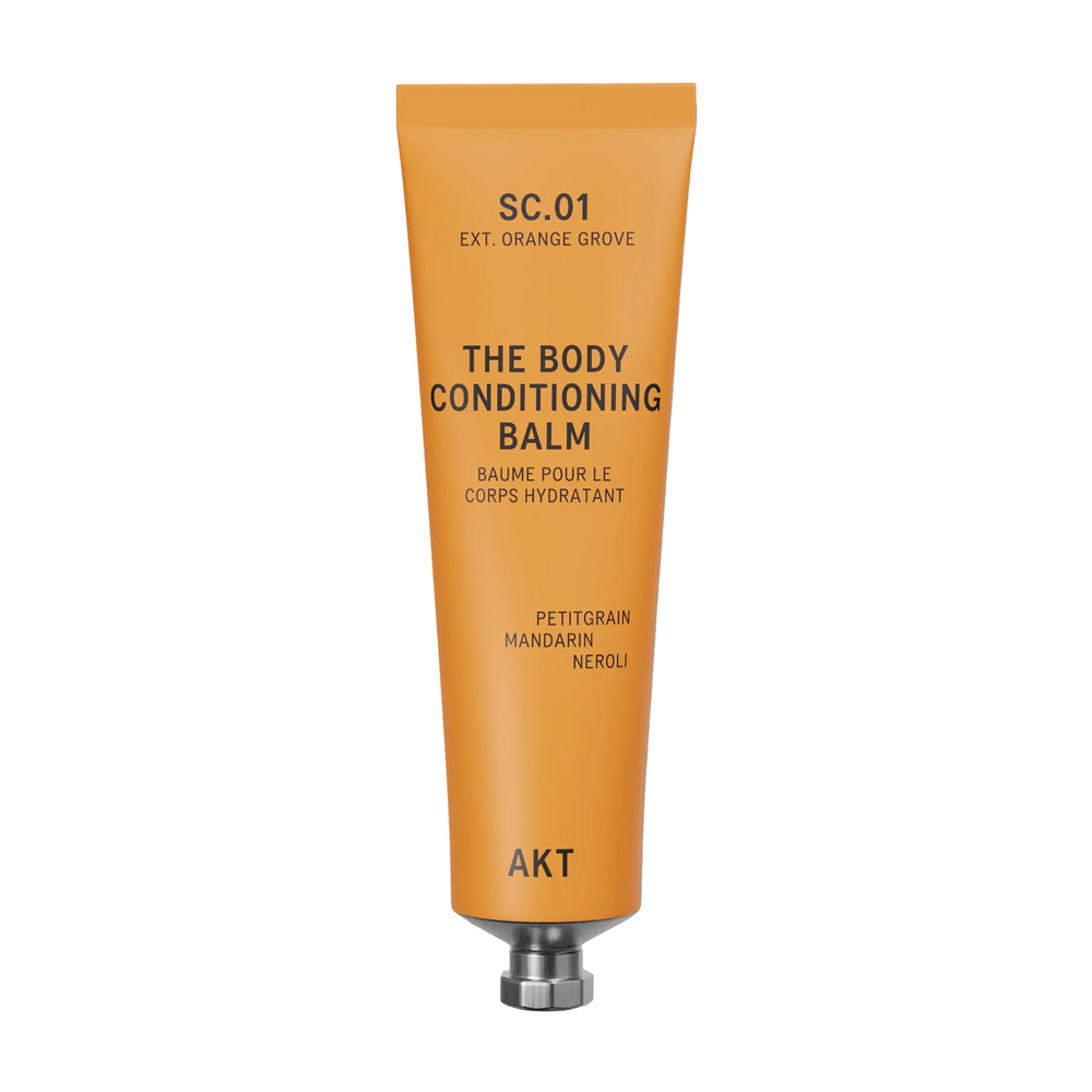 A squeeze tube of AKT London The Body Conditioning Balm in scent 01 ORANGE GROOVE, featuring a vibrant orange body and a metallic silver cap, set against a clean off-white background.