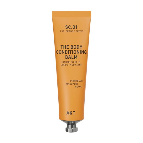 A squeeze tube of AKT London The Body Conditioning Balm in scent 01 ORANGE GROOVE, featuring a vibrant orange body and a metallic silver cap, set against a clean off-white background.
