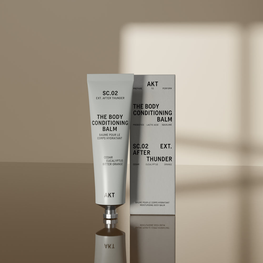 A white squeeze tube of AKT London The Body Conditioning Balm, scent SC.02 After Thunder, with black text on a clean white background.