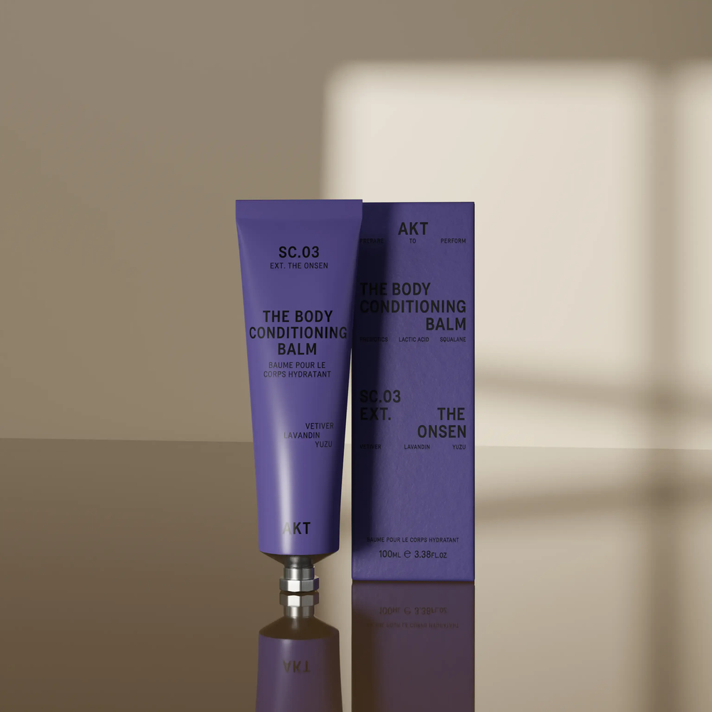 A lavender purple squeeze tube of AKT London The Body Conditioning Balm (SC.03 the Onsen) with a silver metal cap, centered on a light off-white background with a soft shadow.