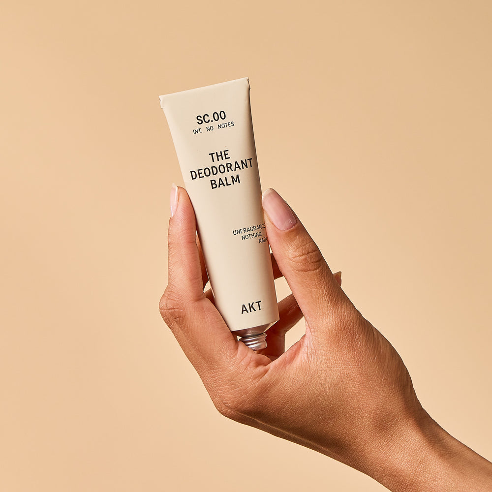 A single tube of deodorant balm by AKT London on a plain white background. The tube is a warm off-white/cream color with black text.
