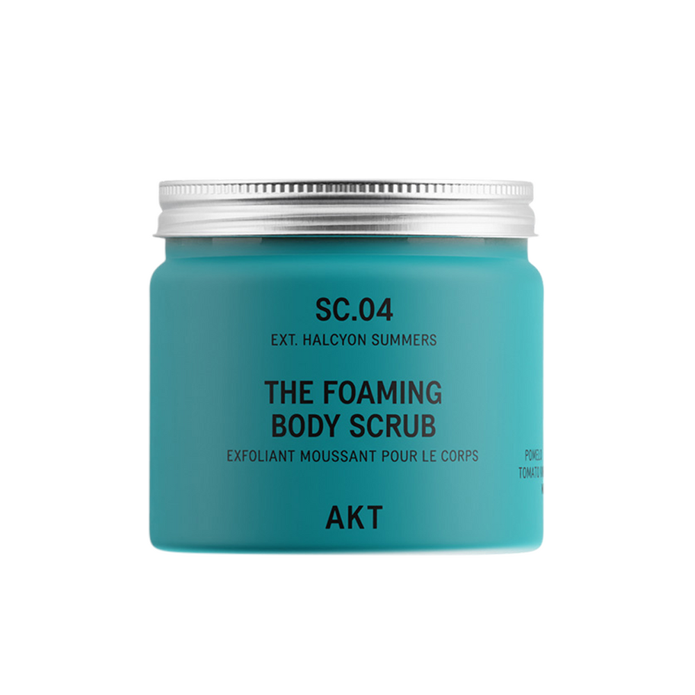 A turquoise blue jar of AKT London The Foaming Body Scrub with a silver metal lid, on a solid white background.