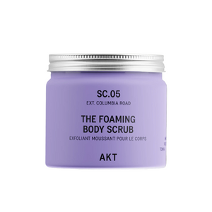 A lavender purple jar of AKT London The Foaming Body Scrub with a silver metal lid, set against a clean off-white background with a soft shadow.