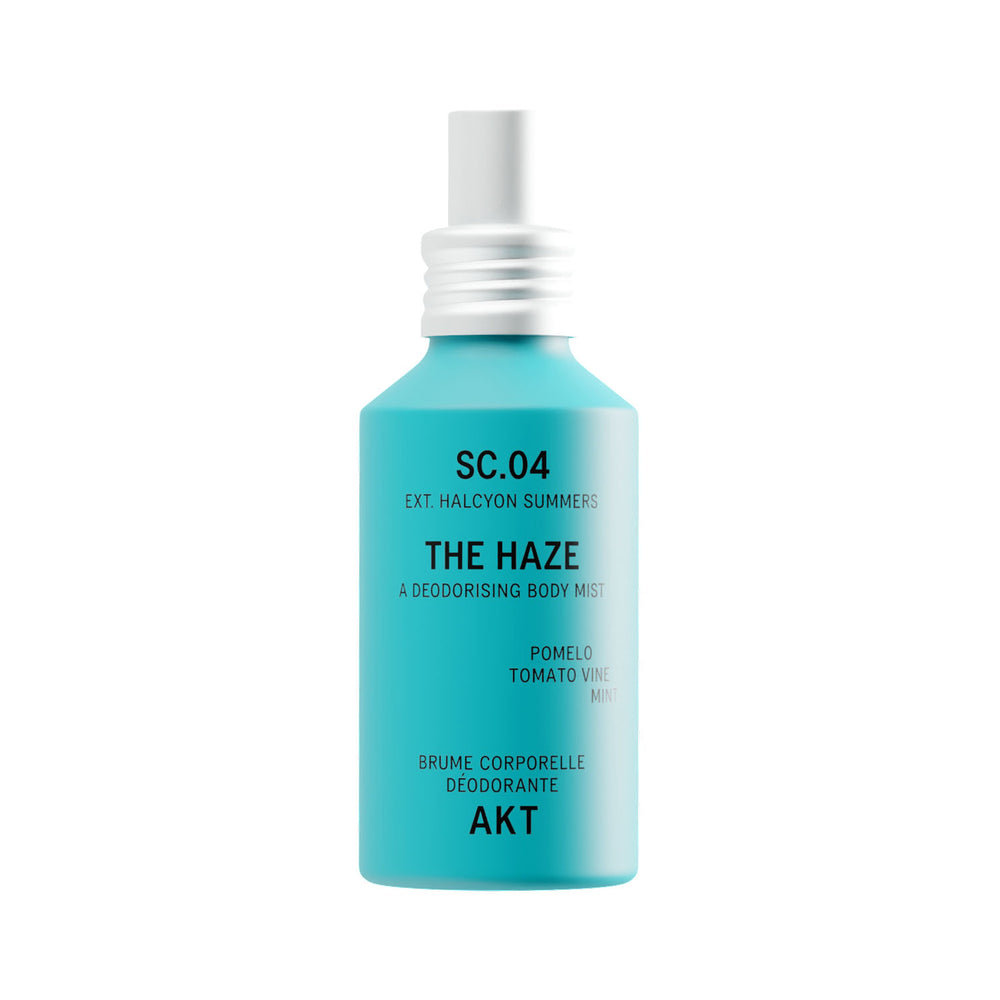 A turquoise spray bottle of body mist with a white cap, labeled 'THE HAZE' by the brand AKT London, on a solid white background.