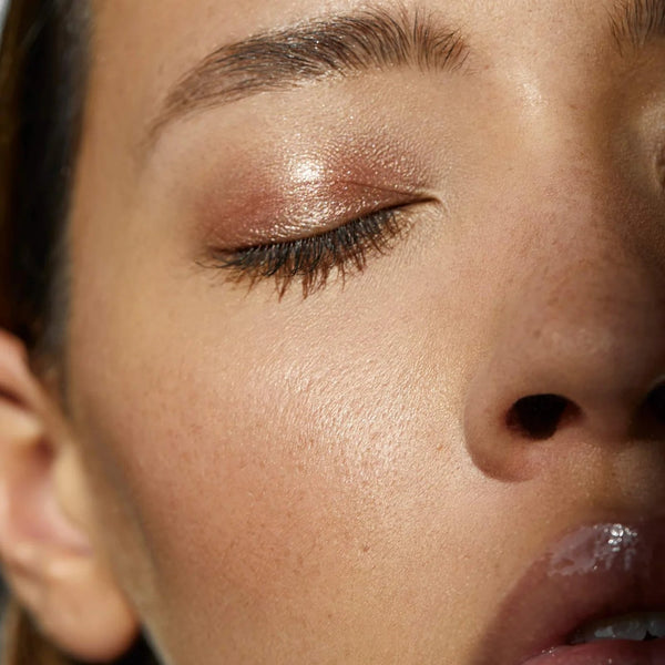 Close-up of a person's face with closed eyes, showcasing a shimmery bronze eyeshadow on the eyelid.