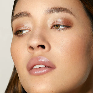 Close-up of a model's face showcasing a shimmery bronze eyeshadow and glossy nude-pink lip color.
