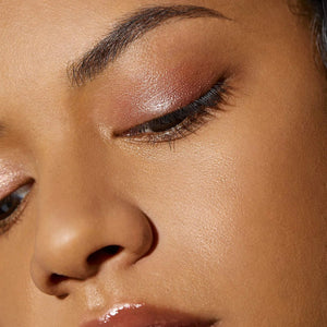 Close-up of a model's eye showcasing a shimmery warm bronze eyeshadow with a subtle pink undertone and dark eyeliner.