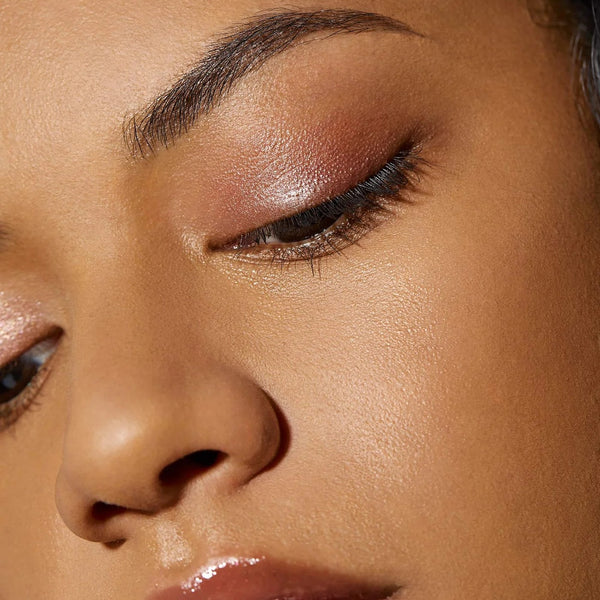 Close-up of a model's eye showcasing a shimmery warm bronze eyeshadow with a subtle pink undertone and dark eyeliner.