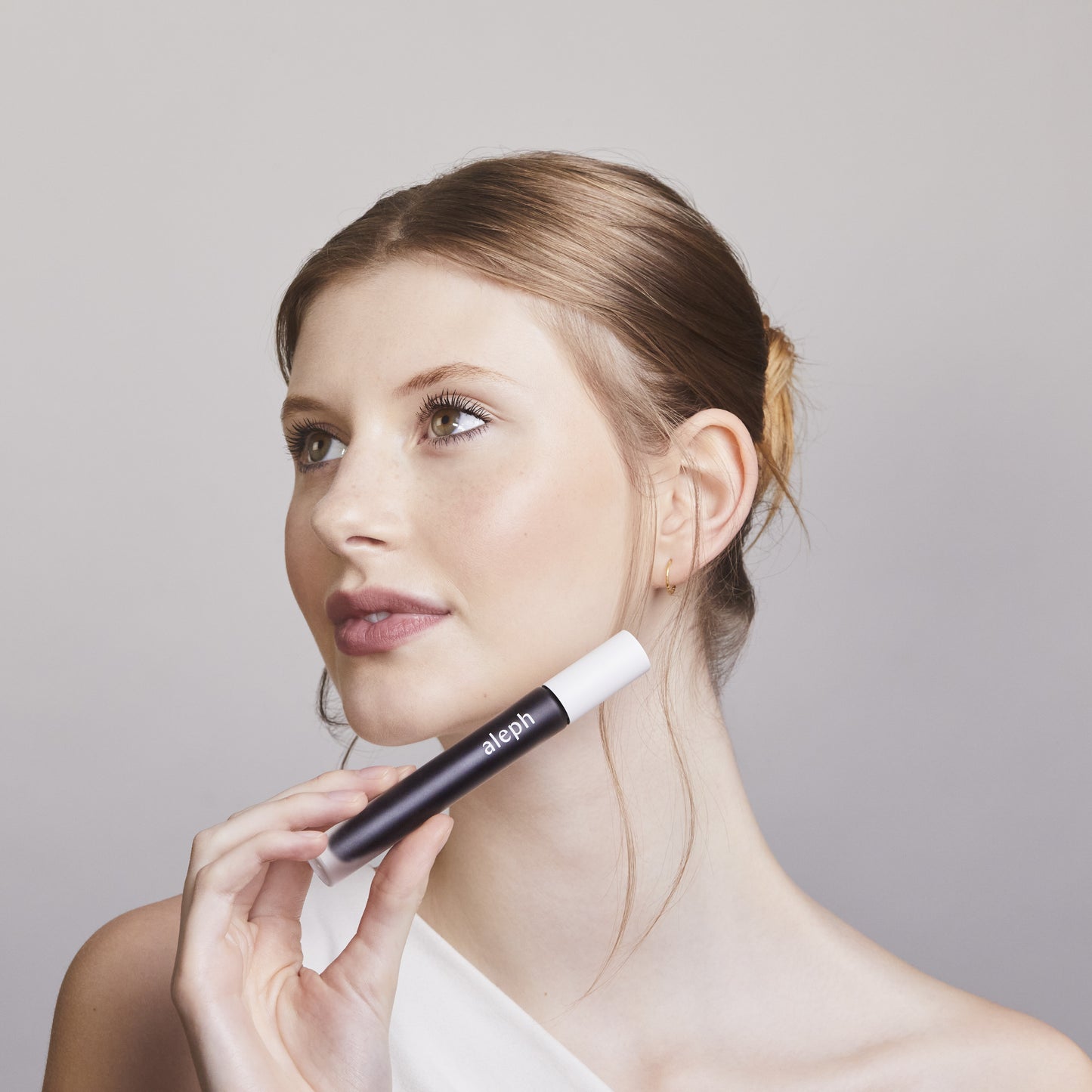 Woman holding a black and white ALEPH Lift / Lengthen Mascara against a plain background