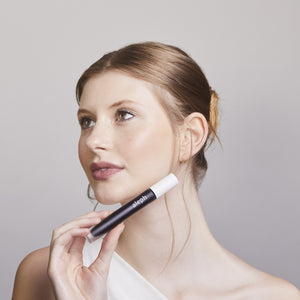 Woman holding a black and white ALEPH Lift / Lengthen Mascara against a plain background