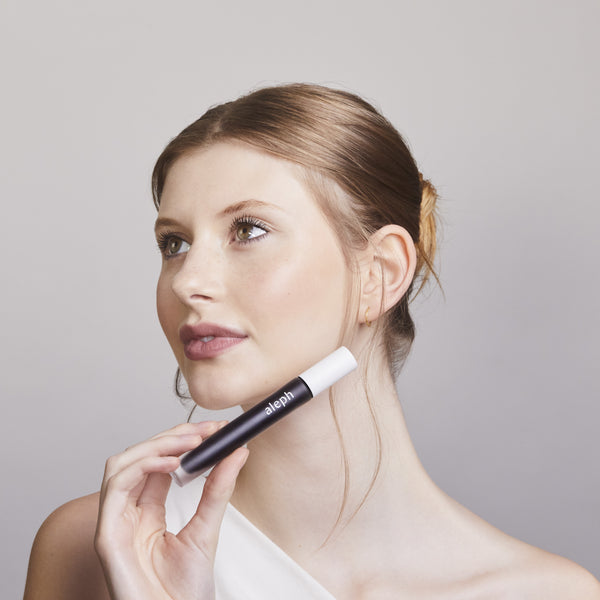 Woman holding a black and white ALEPH Lift / Lengthen Mascara against a plain background