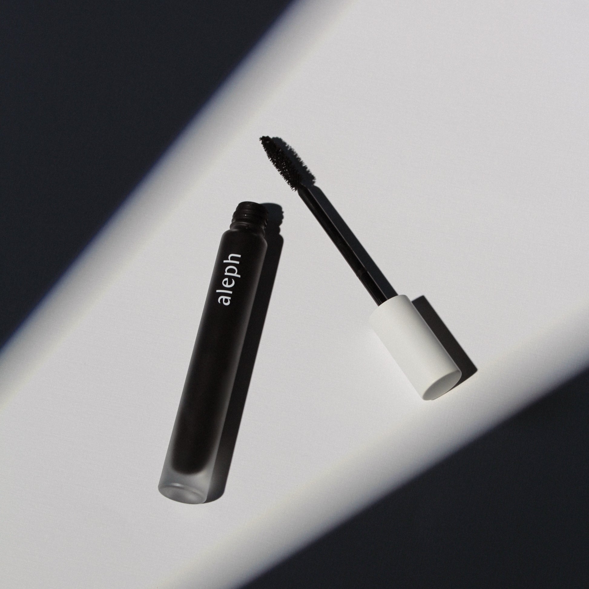 ALEPH Lift / Lengthen Mascara with open cap on a reflective surface
