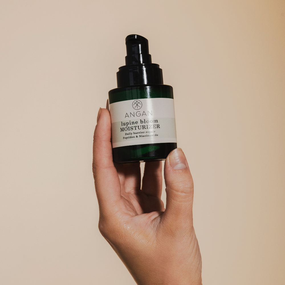 A dark green glass bottle of ANGAN Lupine Bloom Moisturizer with black pump on white background