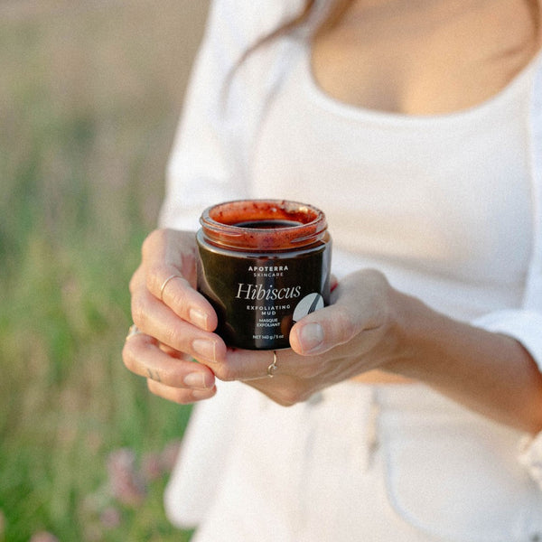 Person holding a jar of Apoterra Hibiscus Exfoliating Mud in a natural setting