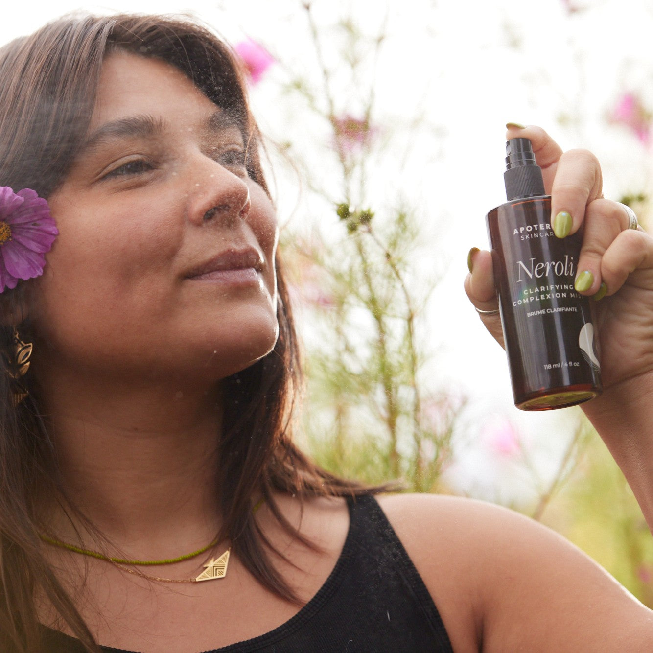 Woman holding a bottle of 'Neroli' face mist with a blurred natural background.  APOTERRA Neroli Clarifying Complexion Mist