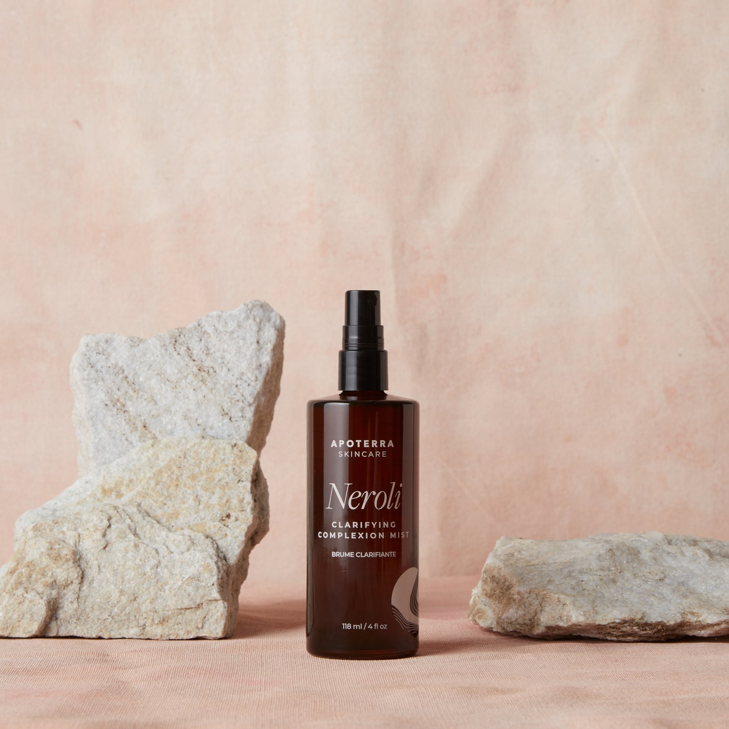 A bottle of Apoterra Skincare Neroli product on a pink background with rocks.