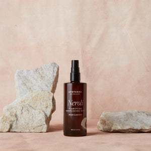 A bottle of Apoterra Skincare Neroli product on a pink background with rocks.