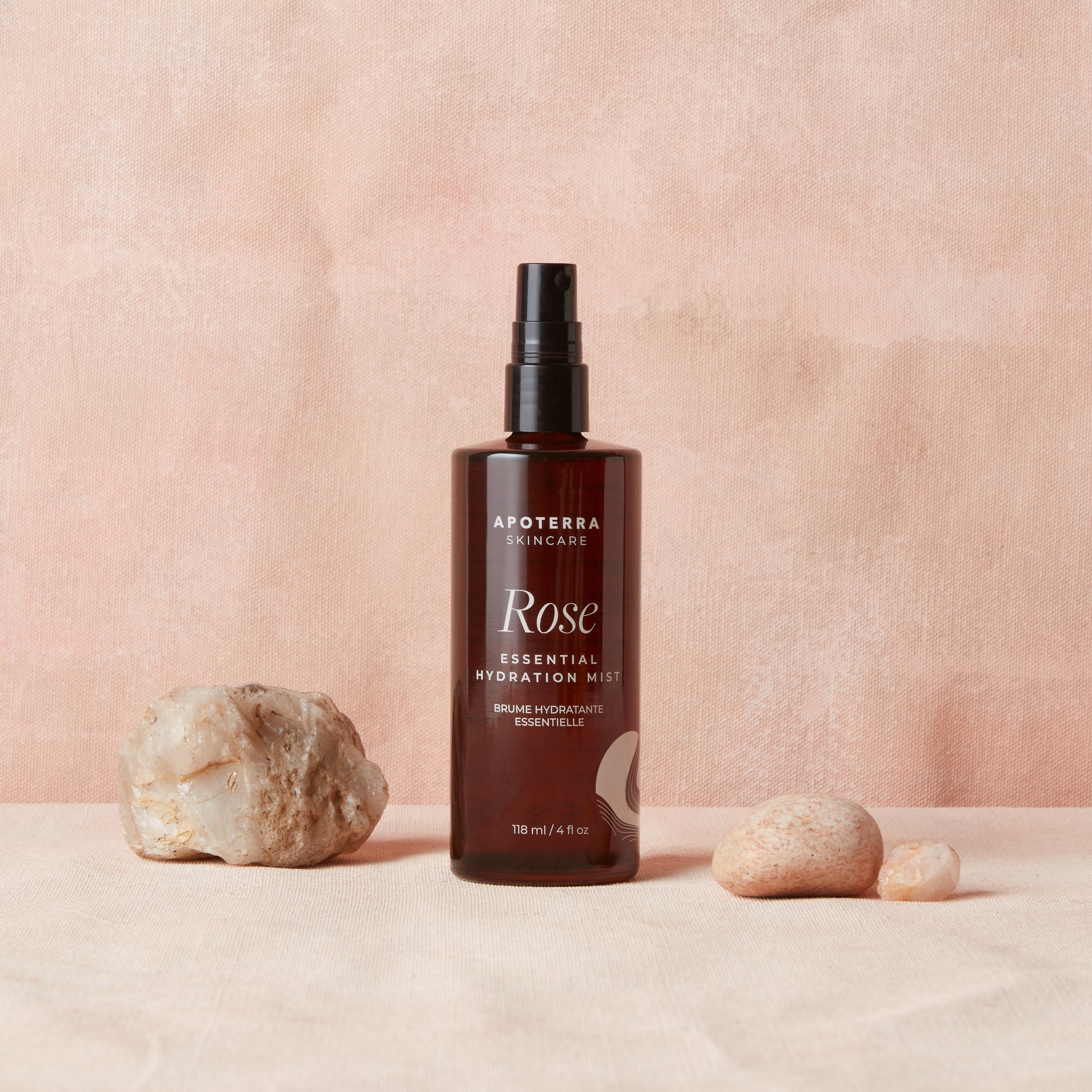 Brown bottle of Apoterra Rose Essential Hydration Mist on a beige background with stones.