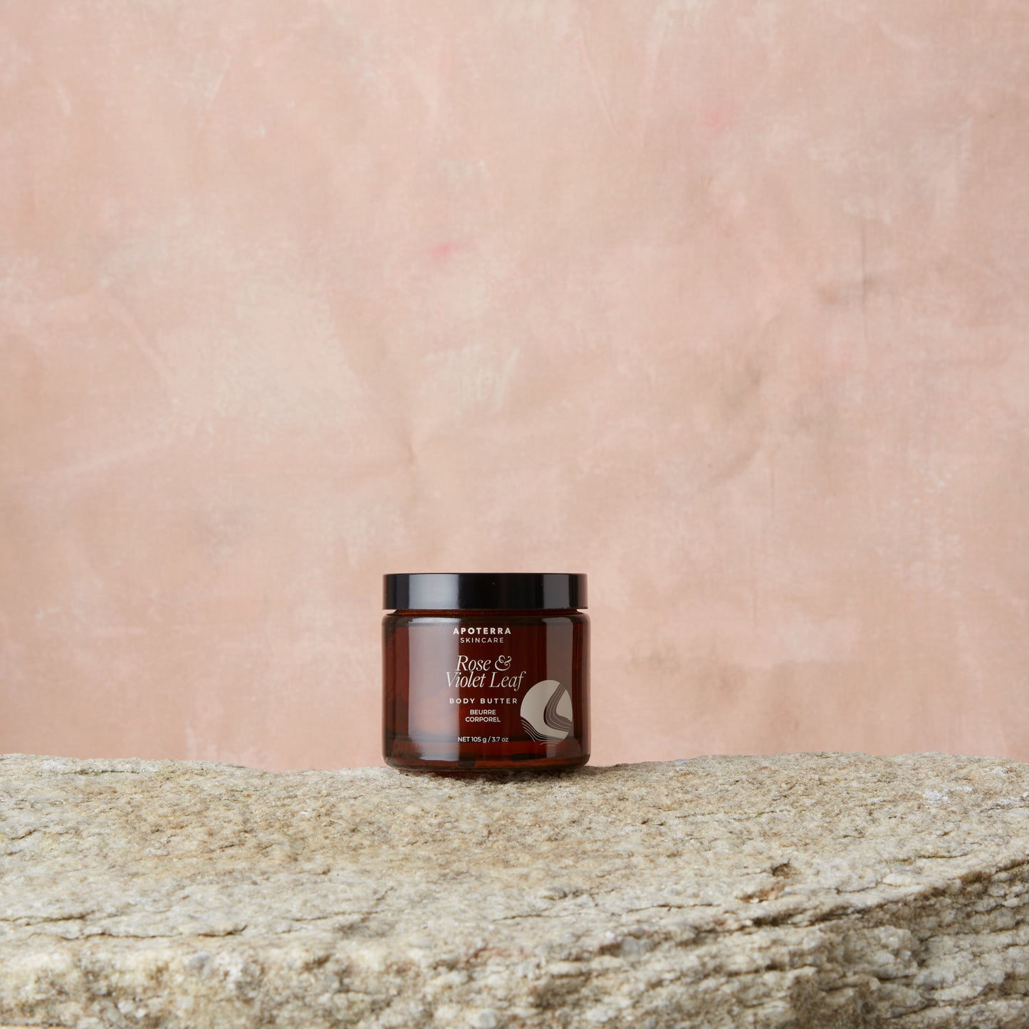 Jar of body butter on a stone surface with a pink textured background. Apoterra Rose & Violet Leaf Body Butter