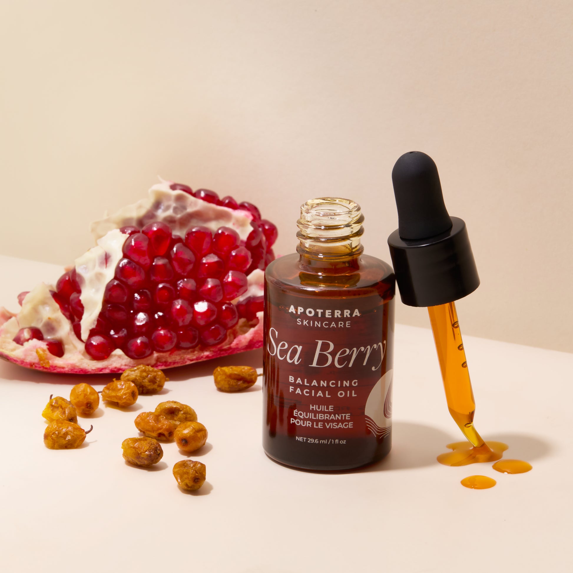 Apoterra Sea Berry Balancing Facial Oil with dropper and pomegranate seeds on a beige background