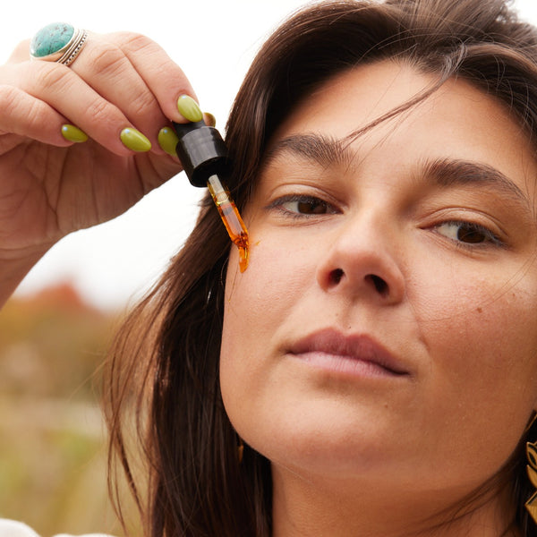 Woman applying a dropper of face oil to her face outdoors. APOTERRA Sea Berry Balancing Facial Oil