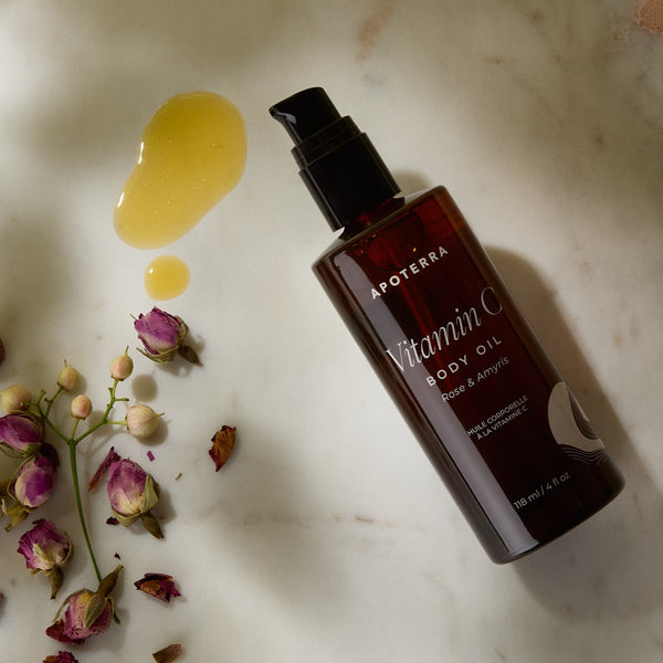 Apoterra Vitamin C Body Oil bottle with droplets and flowers on a marble surface