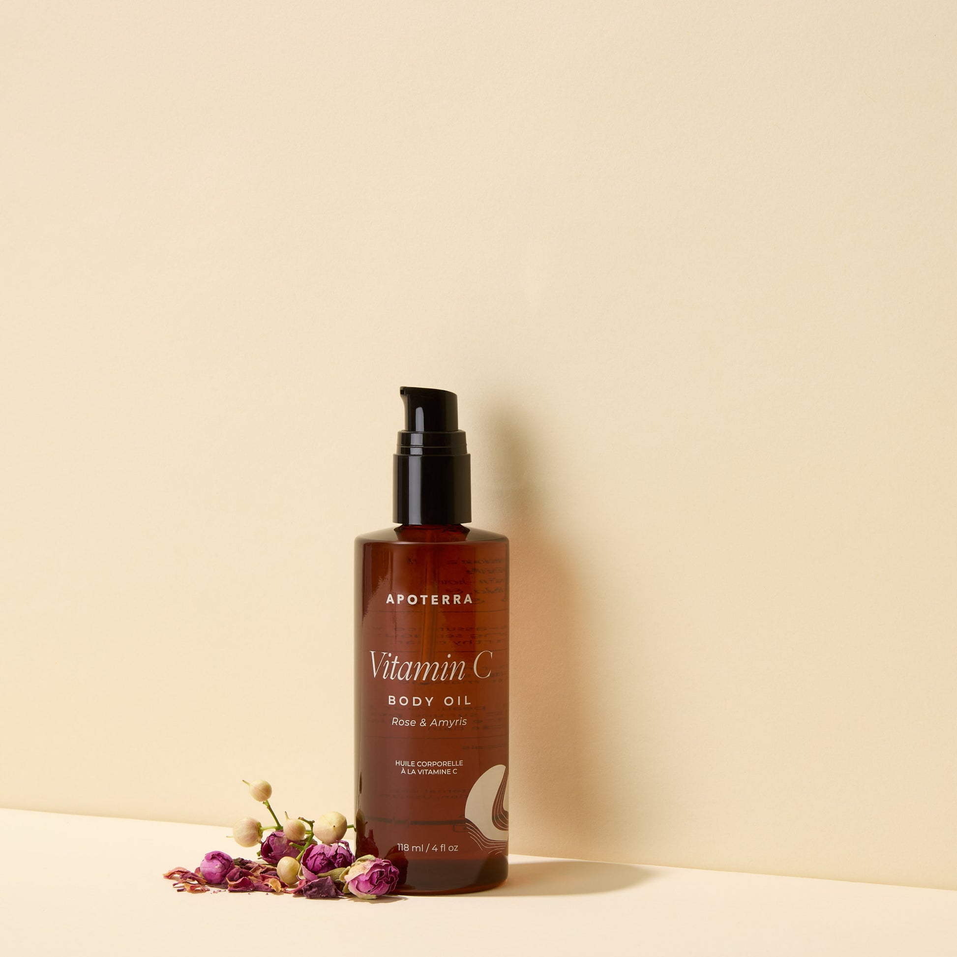 Brown bottle of Apoterra Vitamin C Body Oil on a beige background with dried flowers.