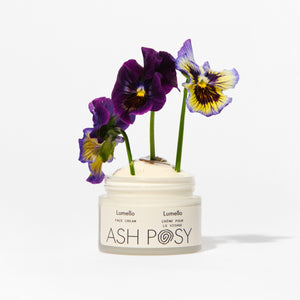 A clear glass jar of Ash Posy face cream with flowers on a white background