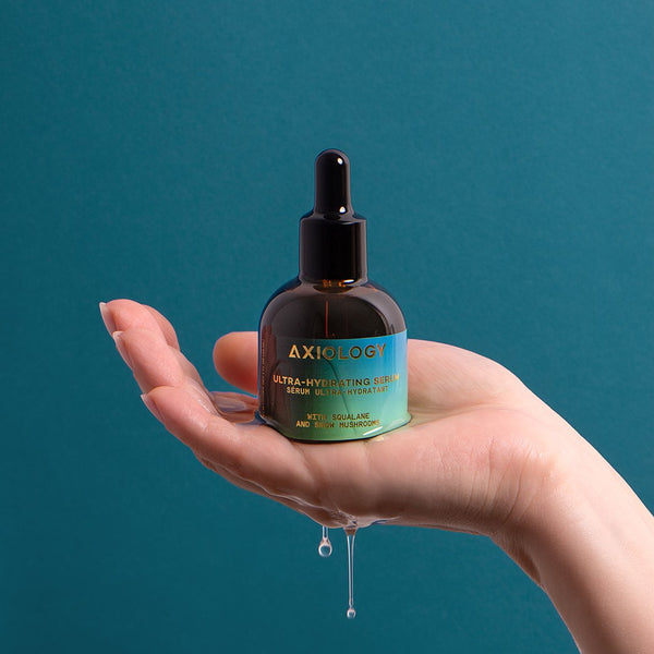 Hand holding a bottle of Axiology serum with a blue background