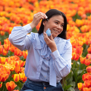 Woman applying BLOOMEFFECTS Royal Tulip Vitamin C Facial Oil in a field of orange tulips