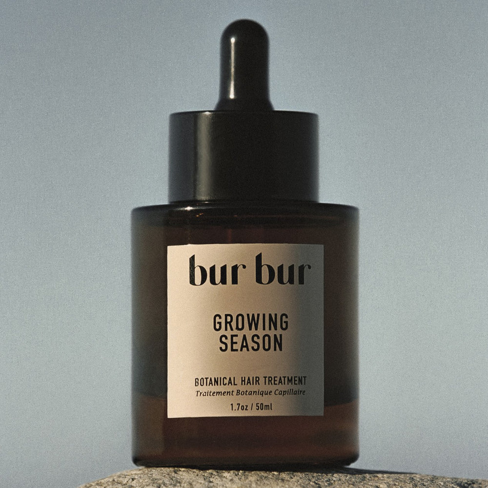 BUR BUR Growing Season Burdock Hair Oil bottle with natural botanical ingredients including burdock root, nettle leaves, and jojoba seeds, on white background.