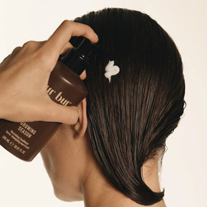 Person applying hair product to their hair with a focus on the product bottle.