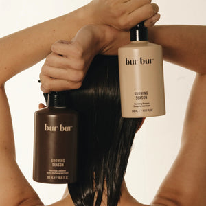 Two bottles of Bur Bur hair care products are held by a woman at the back of hear head. She has wet dark hair.