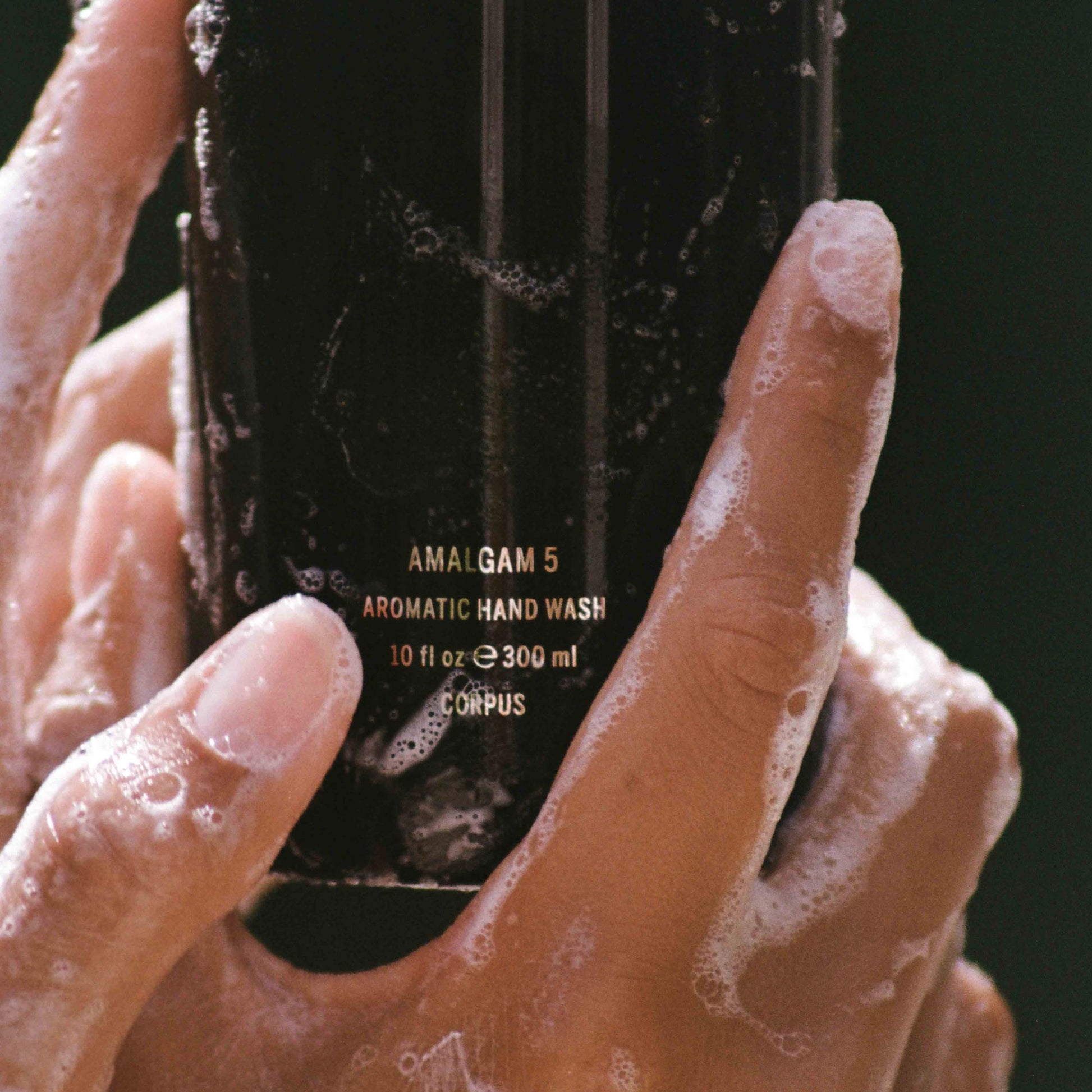 Hand holding a bottle of Amalgam 5 Aromatic Hand Wash with visible foam on hands. CORPUS Aromatic Hand Wash Amalgam 5