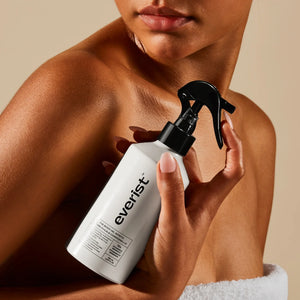 Woman holding a white bottle with black nozzle labeled 'everist' against a beige background