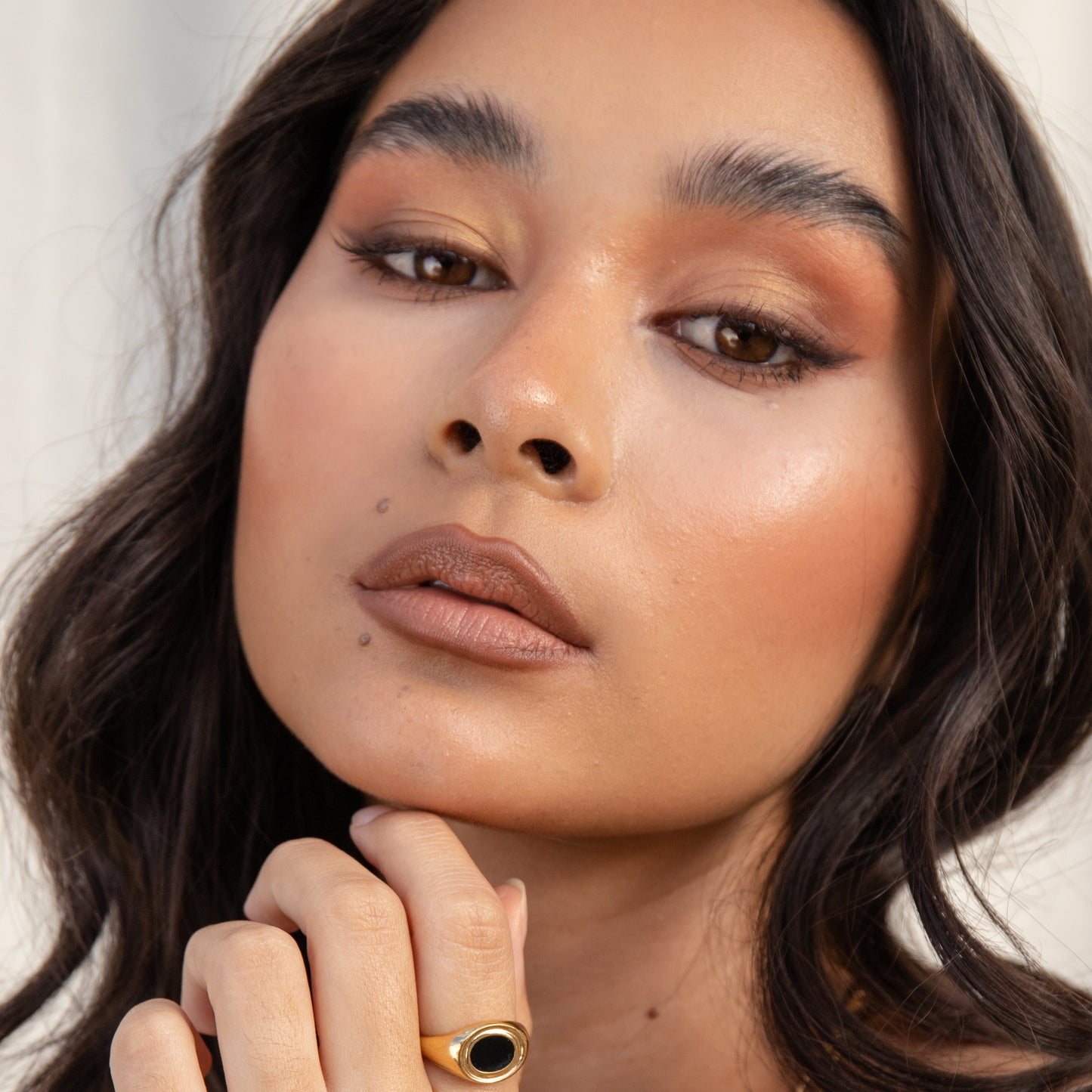 Close-up of a woman with makeup and a gold ring on her finger against a neutral background. EYE OF HORUS Eyeshadow Compact Dawn