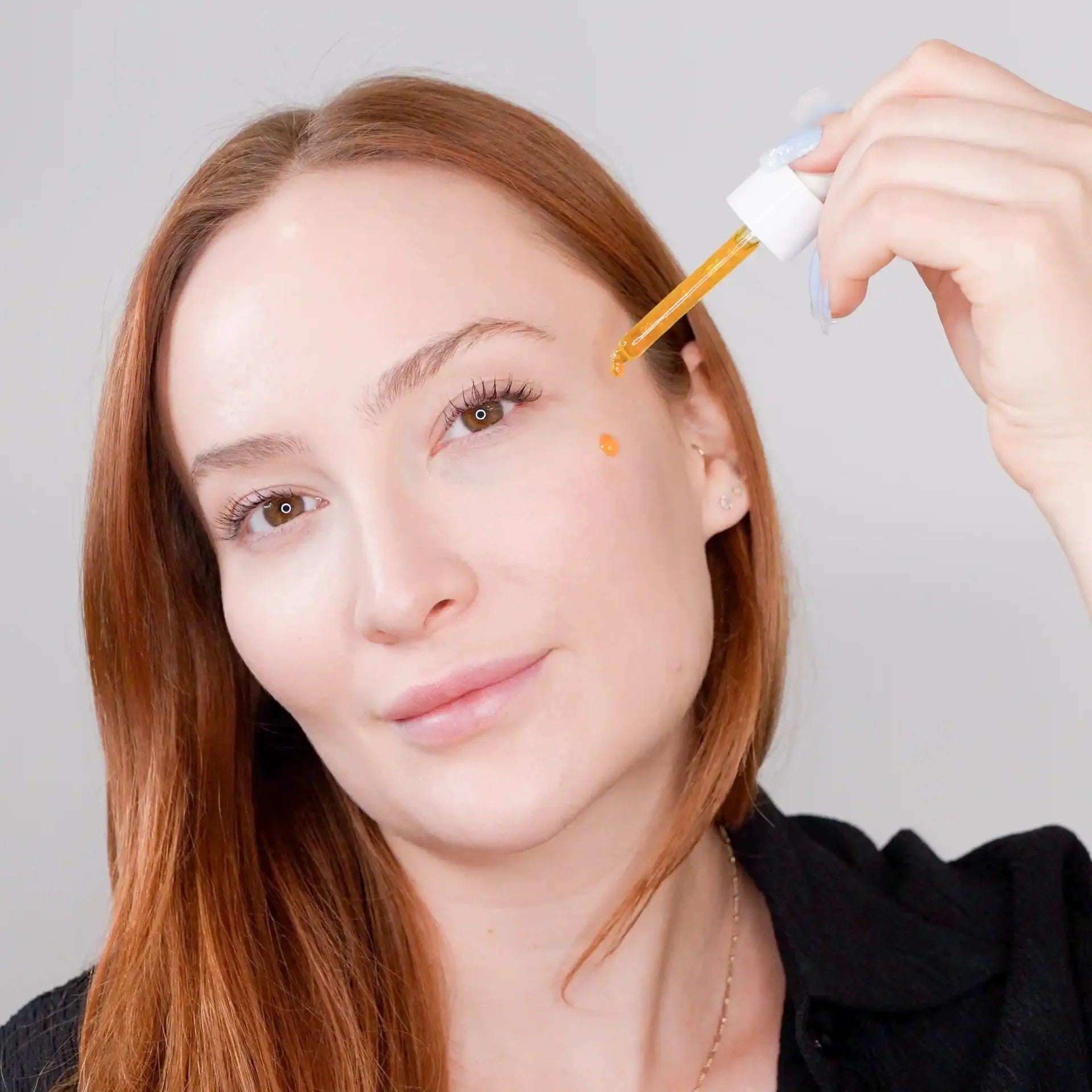 Woman having dropper applied to her face against a neutral background