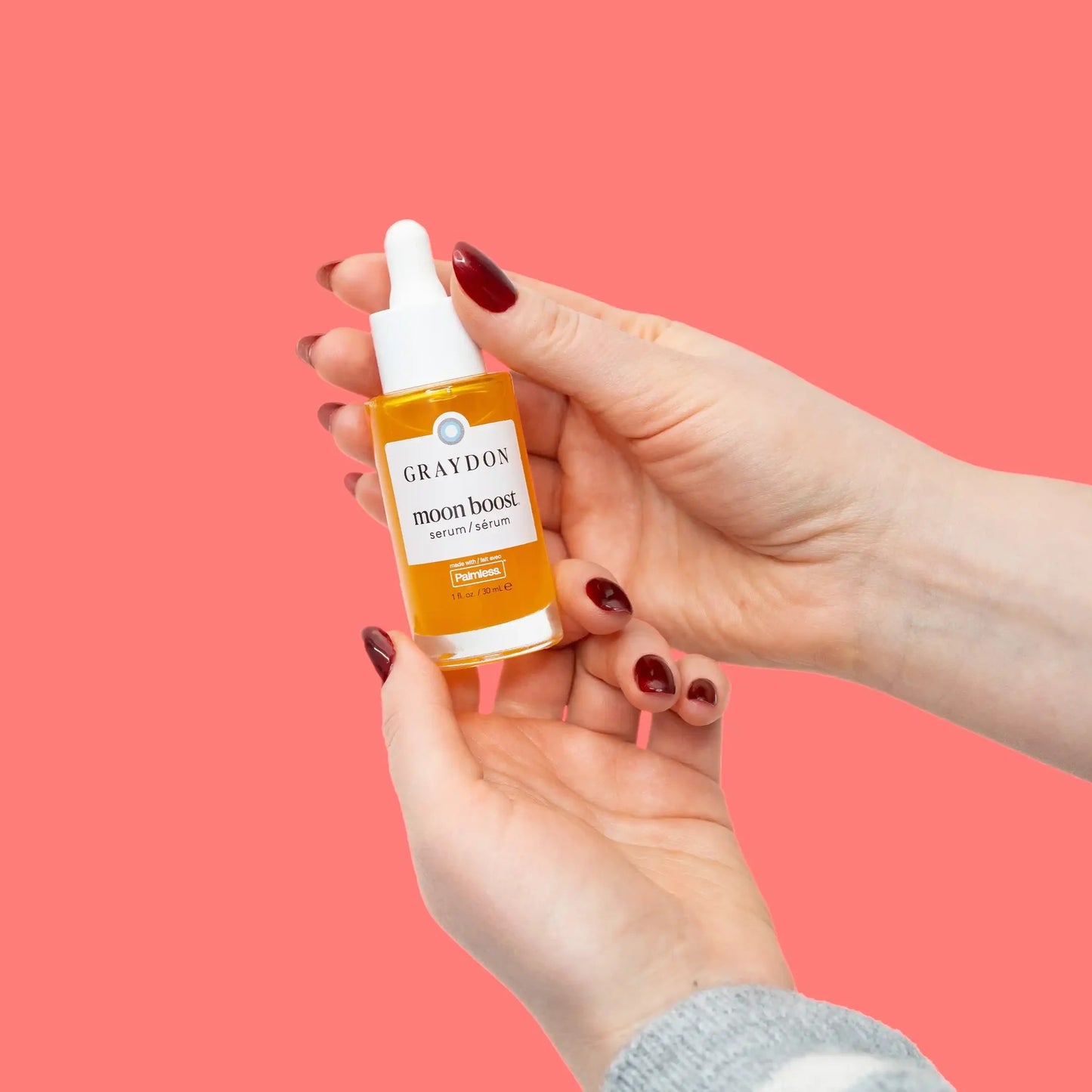 Hand holding a bottle of Graydon moon boost serum against a pink background