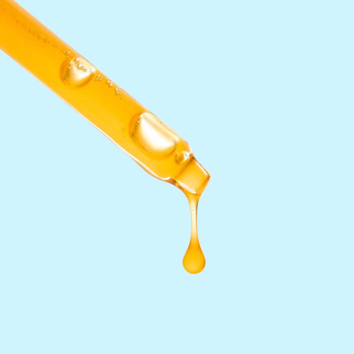 Orange oil dropper with a drop of oil on a light blue background